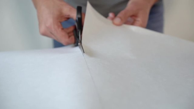 closeup male hands preparing new bended wallpaper roll with scissors on table indoor. Cutting preparation in repair apartment. renovation, design concept