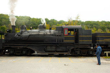 Amish man in color looking over an old steam locomotive