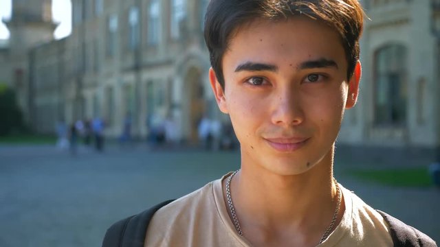 Pretty face of asian man looking at camera in slow motion with urban view behind