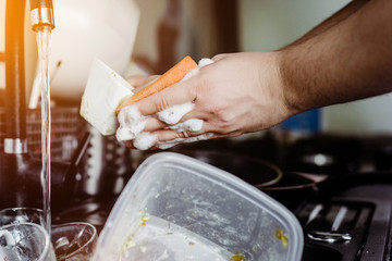 The man cleans the cup after coffee with a scourer. Dirty dishes in the sink. No dishwasher. Concept of caring for dishes in the kitchen. The kitchen sink is full of dirty dishes.