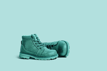 A pair of green leather, children's shoes on a green pastel background. The concept of upcoming cold, selling shoes. A warm, comfortable shoe for children with fur.