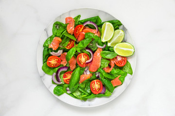 Salmon salad with spinach, cherry tomatoes, red onion, lemon and basil in a plate over white marble background