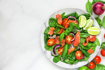 fresh salad with salmon, spinach, cherry tomatoes, red onion and basil in marble plate on white marble table