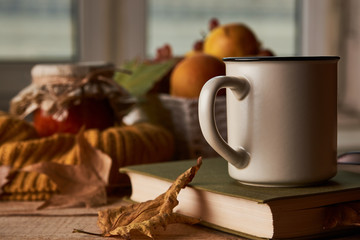 Autumn leaves, cup of coffee, warm scarf, fruits basket and book with glasses on the table. Old wooden table by the window in the autumn beautiful day, close-up