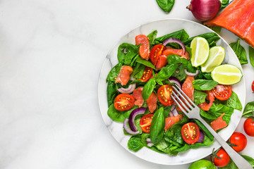 healthy food. fresh salad with salmon, spinach, cherry tomatoes, red onion and basil in marble plate with fork
