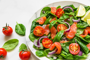 fresh salad with salmon, spinach, cherry tomatoes, red onion and basil in marble plate on white marble table