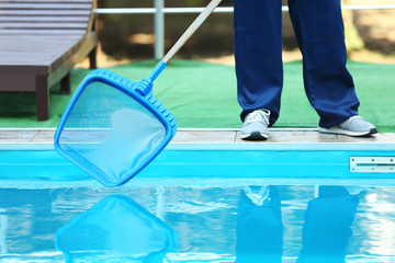 Male worker cleaning outdoor pool with scoop net