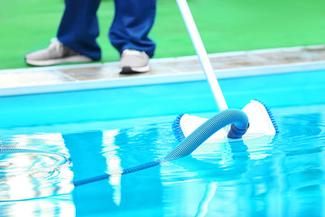 Male worker cleaning outdoor pool with underwater vacuum