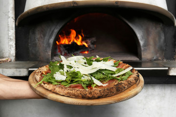 Professional chef holding tasty Italian pizza near oven in restaurant, closeup