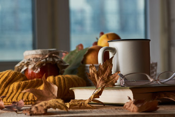 Autumn leaves, cup of coffee, warm scarf, fruits basket and book with glasses on the table. Old wooden table by the window in the autumn beautiful day, close-up