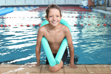Little boy with swimming noodle in indoor pool