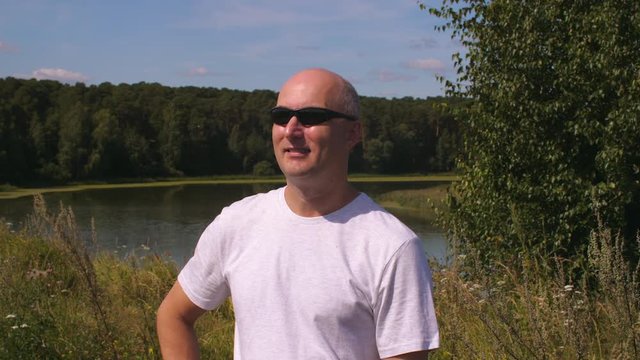 Portrait adult man in sunglasses on background green forest and lake water