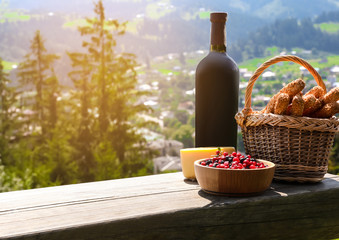 Obraz premium Bottle of red wine and food for picnic on bench against mountain landscape