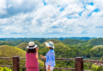 Two girls in hats on the background of the Chocolate hills, Bohol island, Philippines. With selective focus.