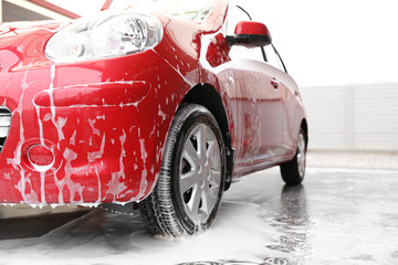 Red auto with foam at car wash. Cleaning service
