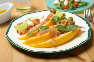 Plate with melon and prosciutto appetizer on wooden table
