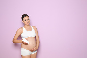 Fototapeta na wymiar Pregnant woman holding body cream on color background with space for text