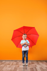 Little boy with red umbrella near color wall