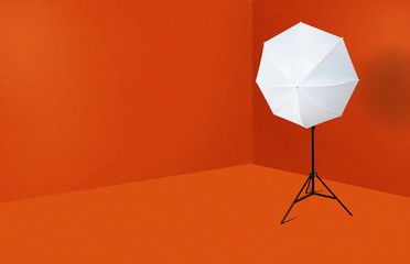 A white umbrella on a photographic stand in an orange room. The concept of photographic equipment,...