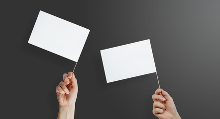 Hands are holding two white, empty flags. Content completion concept. Blank white flag side view. Flags on a dark, black background.