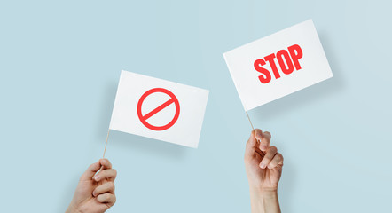 Flags raised up with protest and STOP expression. The concept of protesting, demanding. Hands raise flags up on a blue pastel background.
