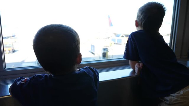 Cute little brothers sit and watch airplanes from the window at the airport