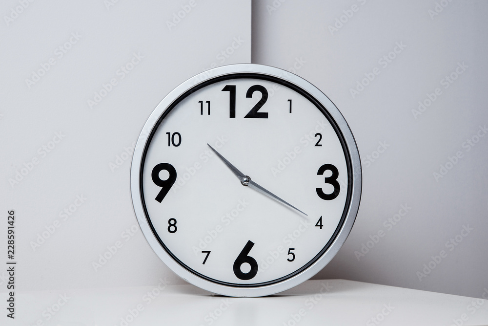Poster a view of a silver, large wall clock. side view of a clock showing the time lying on a white table. 