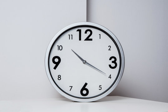 A view of a silver, large wall clock. Side view of a clock showing the time lying on a white table. The concept of passing time, ending work, returning to school and work tasks.