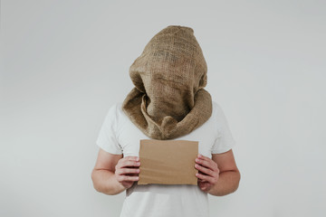 Man with a curtained face on a light background with a cardboard blank board. The concept of...