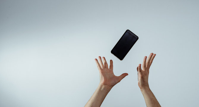 A view of the hand that tosses or catches a mobile phone. The smartphone is falling, hands are trying to catch it. The concept of communication, attempts to connect and talk.