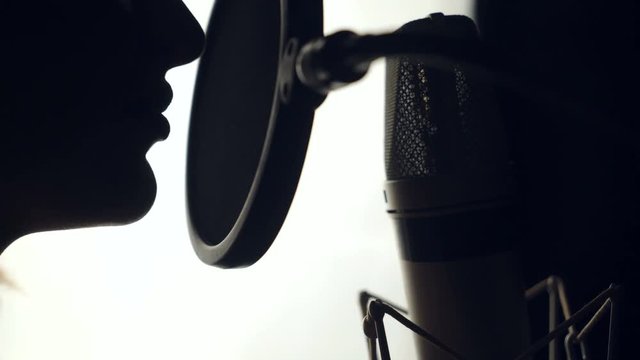 woman is recording a song in an audio studio. The silhouette of a woman's face is singing a song on the white background. Close-up