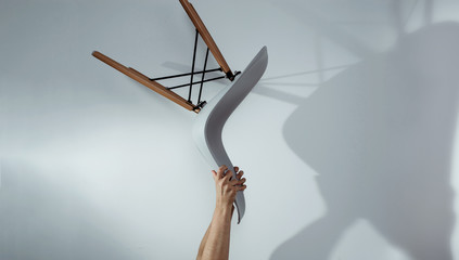 Hands are holding a raised chair on a bright gray background. Man throws a chair, devastates a...