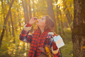 Young woman with nose wiper near autumn tree. Portrait Of Young Woman Sniffing Nasal Spray Closing One Nostril. Woman with allergy symptoms blowing nose.