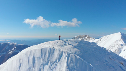 Fototapeta na wymiar AERIAL: Unknown skier hikes up to the top of the snowy mountain in the Alps.