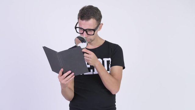 Studio shot of nerd man reading book with magnifying glass