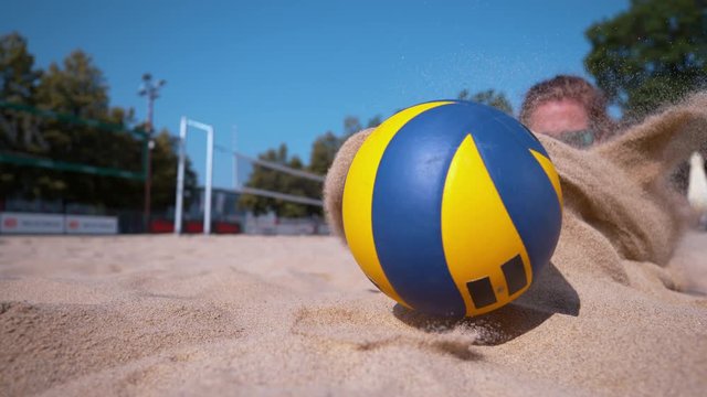 SLOW MOTION, CLOSE UP, DOF: Young Caucasian woman in a bikini dives into sand while trying to score a point during a beach volleyball tournament. Athletic woman on summer vacation playing volleyball.