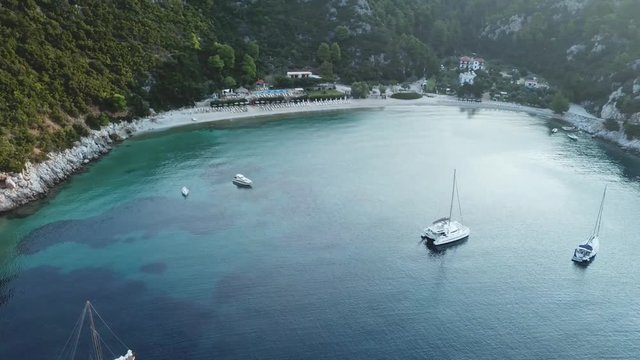 Aerial orbital view of a greek bay with green and bule sea with Sailboats anchored,Early morning sunlight
