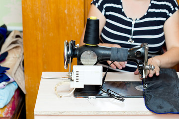 Pretty female tailor sits at table with sewing machine and sews fabric.