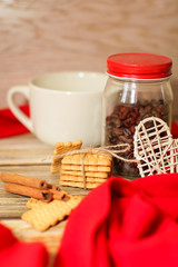 white ceramic Cup with cookie and cinnamon sticks, jar is filled with coffee beans and red scarf. Cozy winter concept