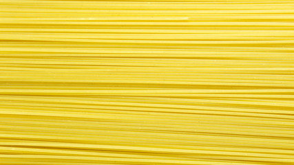 Yellow italian pasta. Long spaghetti. Raw spaghetti waYellow long spaghetti on black background. Thin pasta arranged in rows. Yellow italian pasta. Long spaghetti. Raw spaghetti wallpaper. 