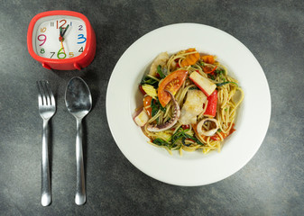 Spaghetti seafood  in a white dish on a black stone floor table. Watch,fork and spoon, Top view with copy space..