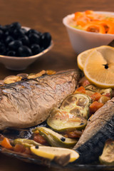 A portion of baked mackerel with vegetables and lemon.