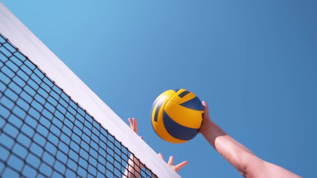 SLOW MOTION, CLOSE UP, LOW ANGLE: Unrecognizable volleyball player strikes the ball with her hand over the net and past the block and scores the point during a summer beach volleyball tournament.