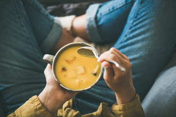 Flat-lay of female in yellow shirt sitting keeping mug of Fall warming pumpkin cream soup with...