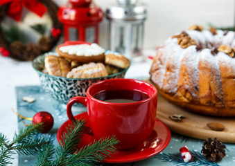 Fruitcake, decor, branches of spruce, plate with a cake and red cup of coffee or tea on the gray wooden table. New year and Christmas decoration concept.  copy space