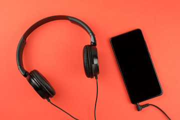 Smartphone mobile phone with headphones. top view red background