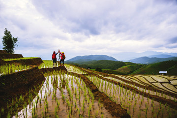 Travel nature lover asian woman and asian man walking take a photo on the field in rainy season.