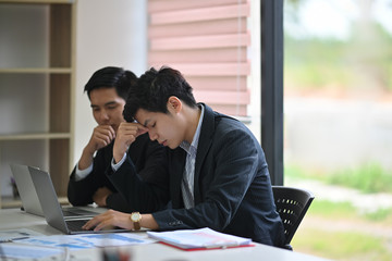 Two Asian colleagues stressed on business paperwork in office