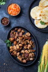 COLOMBIAN FOOD. Fried pork CHICHARRON, AREPAS and colombian tomato sauce. Top view. Black background