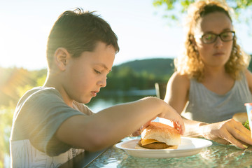 boy eating hamburger outside with his family